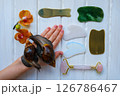 Two achatinas on hand and facial massage kit. Face roller and guasha massager made from natural stones and metal, flat lay. High quality photo Two achatinas on hand and facial massage kit. Face roller and guasha massager made from natural stones and metal, flat lay. High quality photo 126786467