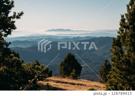 Distant ridgelines with morning mist and layered silhouettes viewed from a mountain meadow Distant ridgelines with morning mist and layered silhouettes viewed from a mountain meadow 126789413