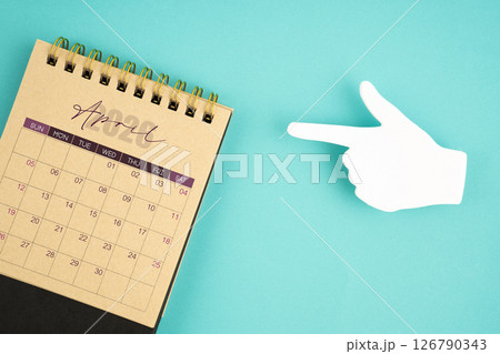 April 2026 calendar from craft paper with paper note finger shape on blue. April 2026 calendar from craft paper with paper note finger shape on blue. 126790343