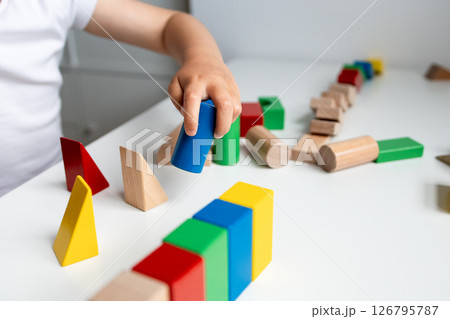 Child playing with colorful geometric wooden blocks on white surface 126795787