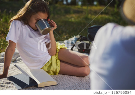 Young Girl Sipping from a Mug While Relaxing Outdoors with a Book 126796084