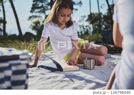 Young Girl Reading a Book During an Outdoor Picnic in the Park Young Girl Reading a Book During an Outdoor Picnic in the Park 126796086