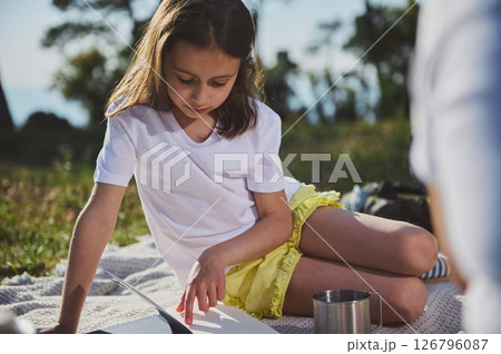 Girl Reading a Book Outdoors During a Sunny Day at a Scenic Picnic Spot Girl Reading a Book Outdoors During a Sunny Day at a Scenic Picnic Spot 126796087