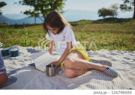 Young Girl Enjoys Reading Outdoors During a Summer Picnic in Scenic Mountain Setting 126796089