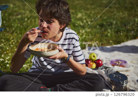 Teen Enjoying a Picnic Lunch in a Scenic Outdoor Setting on a Sunny Day Teen Enjoying a Picnic Lunch in a Scenic Outdoor Setting on a Sunny Day 126796320