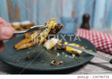 Hand using fork to eat hamburger steak, french fries, and fried egg on a plate 126796716