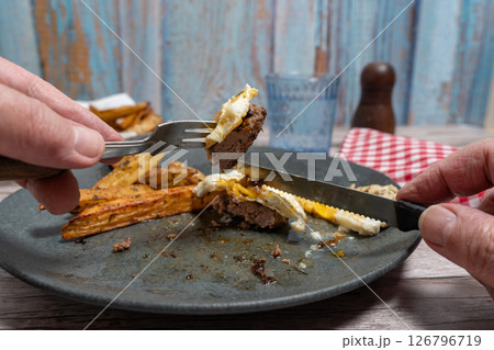Fork Piercing Savory Hamburger Steak Accompanied by Sunny Side Up Egg and Golden Fries on White Plate 126796719