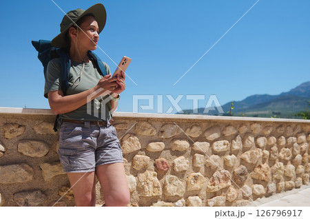 Hiker Relaxing by Stone Wall with Scenic Mountain Views Under Clear Blue Sky 126796917