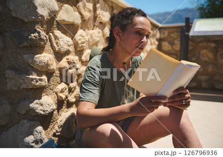 Woman Relaxing Outdoors While Reading a Book on a Sunny Day Woman Relaxing Outdoors While Reading a Book on a Sunny Day 126796936
