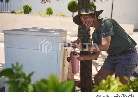 Person Refilling Water Bottle at Outdoor Fountain During A Scenic Day 126796945