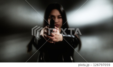 Young woman aiming with a handgun in a blurred background 126797059