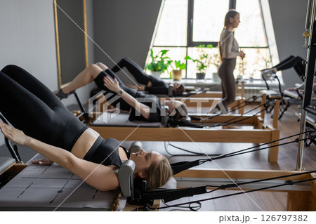 A group of woman exercises Glute bridge on a reformer bed machine in natural sunlight, focusing on pelvis and hips. A group of woman exercises Glute bridge on a reformer bed machine in natural sunlight, focusing on pelvis and hips. 126797382