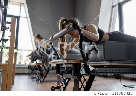 Woman training pilates on the reformer bed. Reformer pilates studio machine for fitness workouts in gym. Fit, healthy and strong authentical body. Fitness concept Woman training pilates on the reformer bed. Reformer pilates studio machine for fitness workouts in gym. Fit, healthy and strong authentical body. Fitness concept 126797429