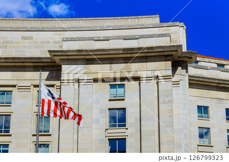 19 April 2025 Washington D.C US Bright sunlight highlights modern architecture of government building, with an American flag proudly waving. 126799323
