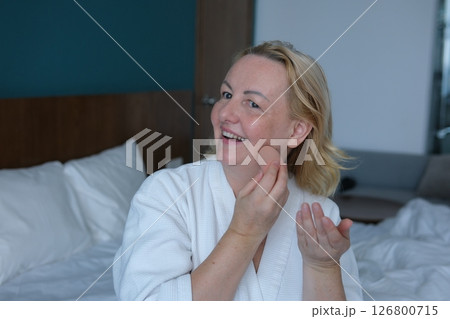apply foundation Focused adult woman sitting at toilet table and looking at reflection in mirror while carefully applying foundation on face during morning makeup 126800715