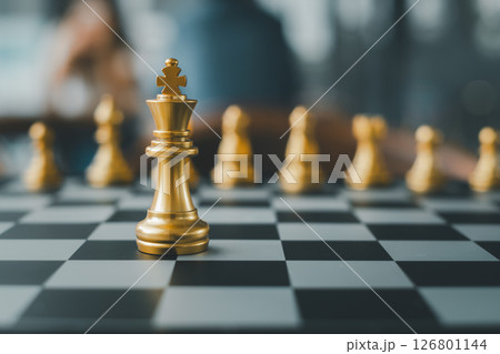 Close-up of golden chess pieces on a chessboard, highlighting the king in a strategic game setting. 126801144