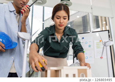 Architectural Planning in Action. Female architect measuring model for sustainable building project. 126803495