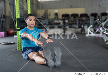 Fitness Focus. Man seated on gym floor, reaching out during a stretching exercise. 126803524