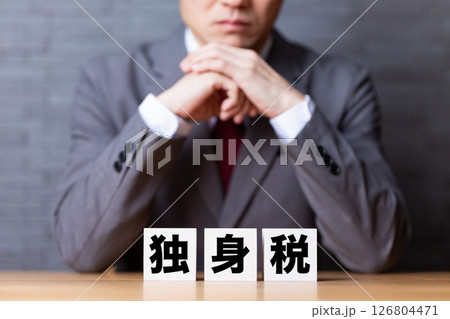 独身税のブロックとスーツを着て悩むミドル男性ビジネスマン 独身税のブロックとスーツを着て悩むミドル男性ビジネスマン 126804471