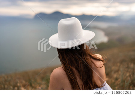 Woman Hat Seascape: Girl views the Black Sea mountains from a grassy hill in Ukraine during daylight. Woman Hat Seascape: Girl views the Black Sea mountains from a grassy hill in Ukraine during daylight. 126805262