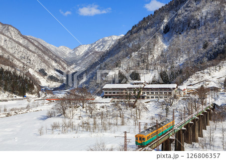 積雪の立山を発車した富山地方鉄道が真川大橋を渡る 126806357