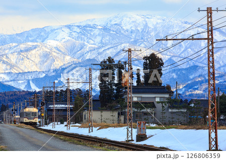 月岡駅に入線する富山地方鉄道に雪に覆われた立山連峰の威容が迫る 126806359