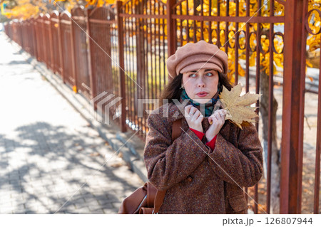 Mid shot of young Caucasian woman wraps herself in a coat with a bouquet of autumn leaves. Autumn city walk. Copy space Mid shot of young Caucasian woman wraps herself in a coat with a bouquet of autumn leaves. Autumn city walk. Copy space 126807944