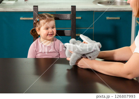 Happy toddler girl exploring toy with guidance from mother at home table. Concept of curiosity, preschool education, and emotional safety Happy toddler girl exploring toy with guidance from mother at home table. Concept of curiosity, preschool education, and emotional safety 126807993