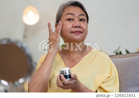 Beauty and Age Diversity. A senior woman applying cream with a confident expression, embracing her beauty. 126811831