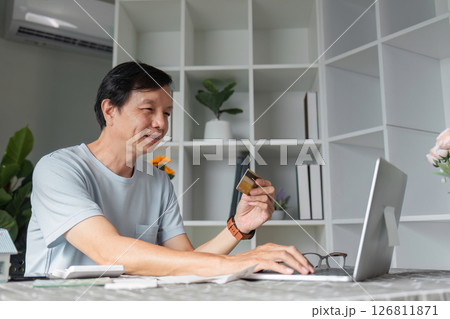 Focused man completing online purchase with credit card at desk using laptop Focused man completing online purchase with credit card at desk using laptop 126811871