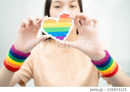 Asian woman holding LGBT heart with rainbow flag. 126813125
