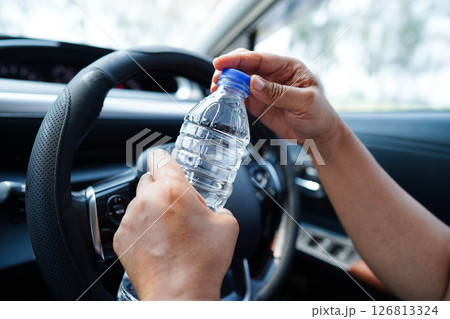 Asian woman driver hold cold water for drink in car, dangerous and risk an accident. 126813324