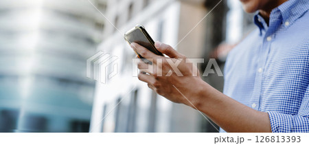 A man using a smartphone in an urban environment, representing mobile communication, digital lifestyle, and business on the go 126813393