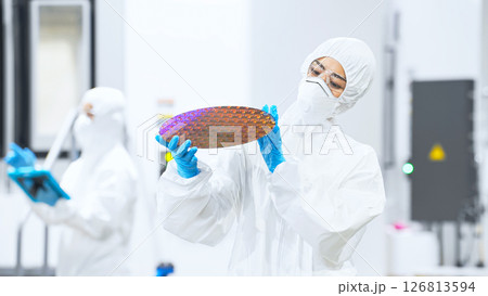 半導体工場でシリコンウエハーを検査する防護服を着た女性作業員 半導体工場でシリコンウエハーを検査する防護服を着た女性作業員 126813594