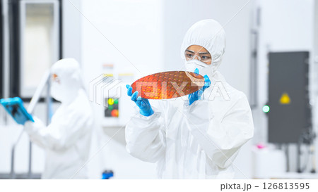 半導体工場でシリコンウエハーを検査する防護服を着た女性作業員 半導体工場でシリコンウエハーを検査する防護服を着た女性作業員 126813595