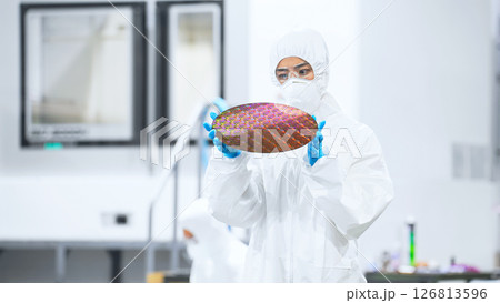 半導体工場でシリコンウエハーを検査する防護服を着た女性作業員 126813596