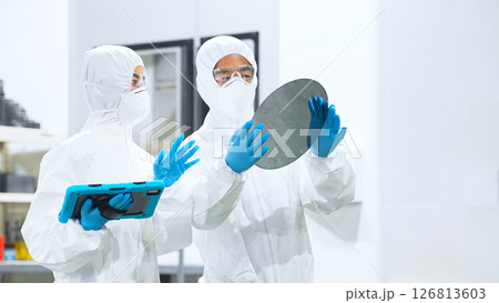 半導体工場でタブレットを持ってシリコンウエハーを検査する防護服を着た男女作業員 半導体工場でタブレットを持ってシリコンウエハーを検査する防護服を着た男女作業員 126813603