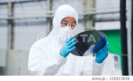 半導体工場でシリコンウエハーを検査する防塵服を着た男性作業員 126813636