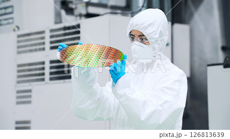 半導体工場でシリコンウエハーを検査する防塵服を着た女性作業員 126813639