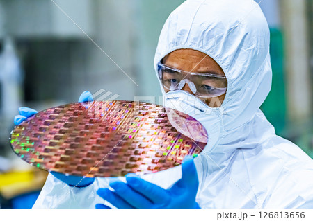 半導体工場でシリコンウエハーを検査する防護服を着た男性作業員 126813656