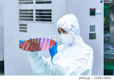 半導体工場でシリコンウエハーを検査する防護服を着た女性作業員 半導体工場でシリコンウエハーを検査する防護服を着た女性作業員 126813662