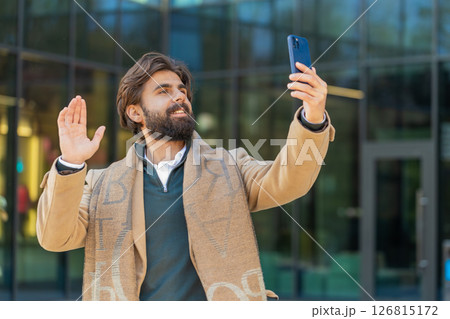 Indian man blogger taking selfie on smartphone video call online with subscribers on city street 126815172