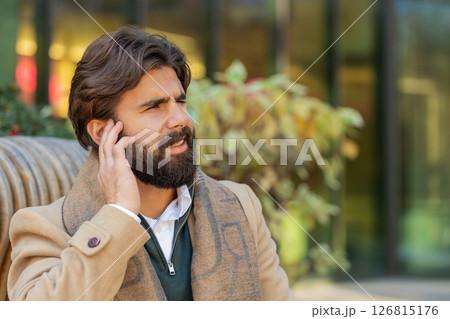 Indian young business man suffers from earache, ear pain, infection, inflammation on city street 126815176
