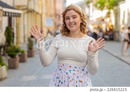 Redhead woman smiling friendly at camera, waving hands hello, hi, greeting or goodbye in city street 126815223