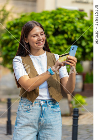 Happy Caucasian woman using credit card smartphone while purchases online shopping on city street Happy Caucasian woman using credit card smartphone while purchases online shopping on city street 126815338