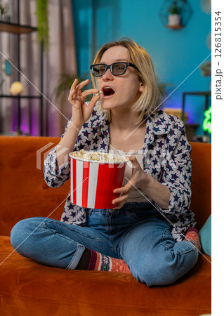Excited young woman sitting on couch eating popcorn and watching interesting TV serial film game 126815354