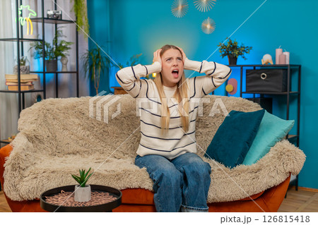 Caucasian woman irritated by noisy neighbors covering ears on sofa construction music loud indoors Caucasian woman irritated by noisy neighbors covering ears on sofa construction music loud indoors 126815418