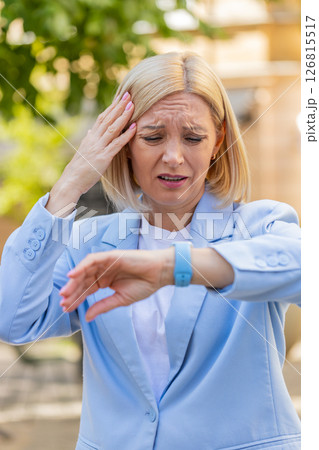Shocked mature woman businesswoman in hurry checking time on smartwatch walking on city street Shocked mature woman businesswoman in hurry checking time on smartwatch walking on city street 126815517