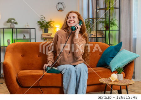 Smiling young woman making wired telephone call conversation with friends sitting on sofa at home 126815548