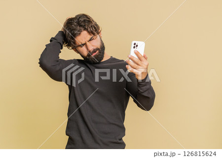 Upset Lebanese young man using mobile cell phone typing browsing, loses lottery on beige background Upset Lebanese young man using mobile cell phone typing browsing, loses lottery on beige background 126815624